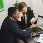 Two business professionals working on growth charts using laptop in an office setting.